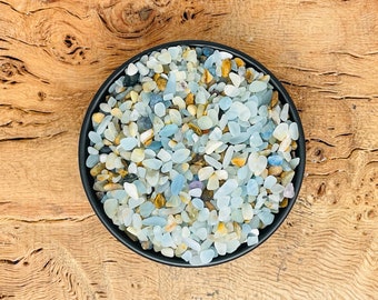 Puede incluir: Un cuenco negro lleno de pequeñas piedras de color azul claro, blanco y marrón. Las piedras son lisas y pulidas, y parecen ser naturales.
