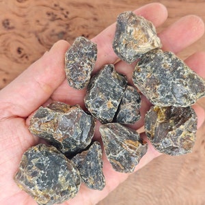 May include: A collection of dark amber stones with a variety of shapes and sizes. The stones have a rough, natural texture and a dark, opaque color.