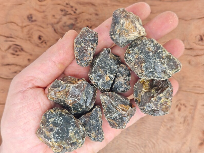 May include: A collection of dark amber stones with a variety of shapes and sizes. The stones have a rough, natural texture and a dark, opaque color.