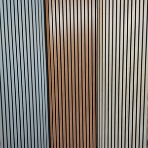 Può includere: Tre pannelli verticali di rivestimento murale a doghe di legno. I pannelli sono di colori diversi: grigio chiaro, marrone e beige chiaro. Ogni pannello presenta linee verticali nere che corrono tra le doghe di legno.