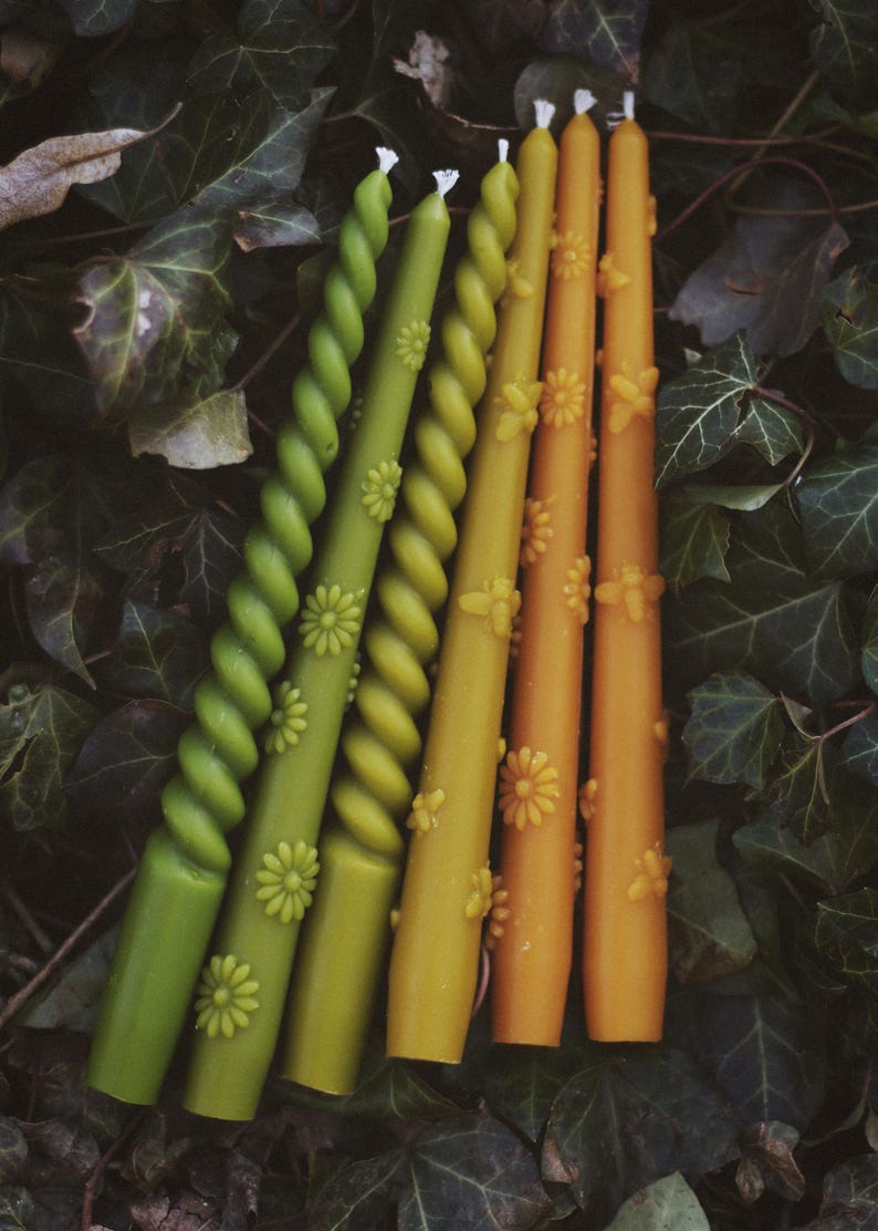 May include: A set of six taper candles in shades of green and yellow. Three candles feature a twisted spiral design with embossed daisy motifs, while the other three are smooth, straight cylinders decorated with embossed bee and daisy patterns.