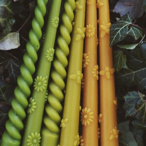 May include: A collection of six taper candles in shades of green and yellow. Three candles feature a twisted spiral design, while the other three are smooth and decorated with embossed floral and bee motifs along their length.
