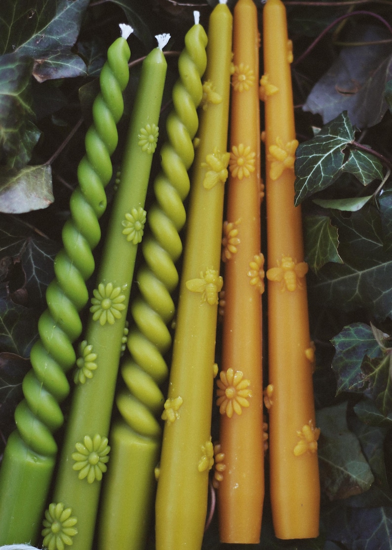 May include: A collection of six taper candles in shades of green and yellow. Three candles feature a twisted spiral design, while the other three are smooth and decorated with embossed floral and bee motifs along their length.