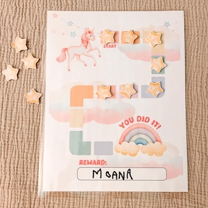 May include: A reward chart featuring a unicorn illustration, stars, and the text "YOU DID IT!". The chart has a rainbow and clouds design, with the name "MOANA" written in a box. Includes several star-shaped stickers.