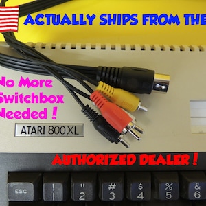May include: A close-up of an Atari 800 XL computer with a black and white keyboard. The computer has a label that reads "No More Switchbox Needed!" and "AUTHORIZED DEALER!"  The computer is connected to a set of three RCA cables, one yellow, one red, and one white.