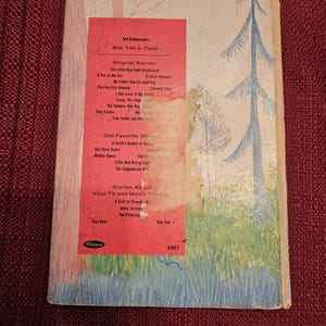 Op de afbeelding: Vintage Whitman "Big Tell-a-Tales" boek. De omslag toont een grillige illustratie van een bossc&egrave;ne met bomen en gras. De titel van het boek en een lijst met verhalen zijn zichtbaar.
