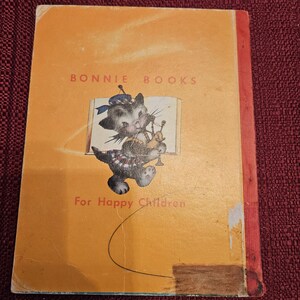 May include: A yellow book with the title "BONNIE BOOKS" and the text "For Happy Children". The cover features a cartoon cat wearing a kilt and playing the bagpipes.