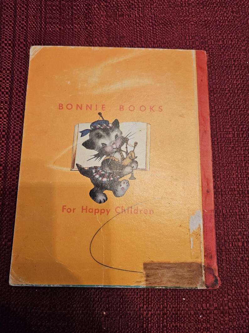 May include: A yellow book with the title "BONNIE BOOKS" and the text "For Happy Children". The cover features a cartoon cat wearing a kilt and playing the bagpipes.