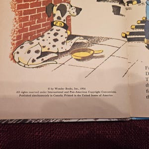 May include: A black and white Dalmatian dog wearing a red collar with the letters "F.D." on it. The dog is lying down on a brick sidewalk with a yellow metal bowl next to it. The text "&copy; by Wonder Books, Inc., 1956" is at the bottom of the page.