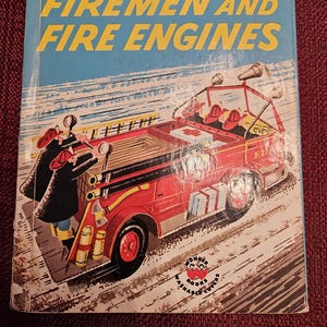 May include: A vintage children's book cover featuring a red fire engine with firefighters rushing to a scene. The book is titled "The Wonder Book of Firemen and Fire Engines" and has a price of 39 cents.