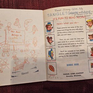 May include: An open book with a red inscription that says "This Book Belongs to Scott Fannel". The book is titled "Tangleton Tales" and has illustrations of animals and a football.