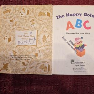 May include: A vintage children's book titled "The Happy Golden ABC" illustrated by Joan Allen. The cover features a colorful illustration of the letters A, B, and C, and a child in a red and white hat peeking out of a box.