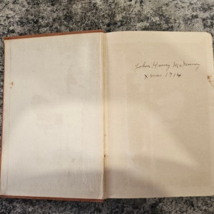Puede incluir: Primer plano del interior de la cubierta de un libro con una inscripci&oacute;n manuscrita que dice "John Henry McKinney X-mas 1914".