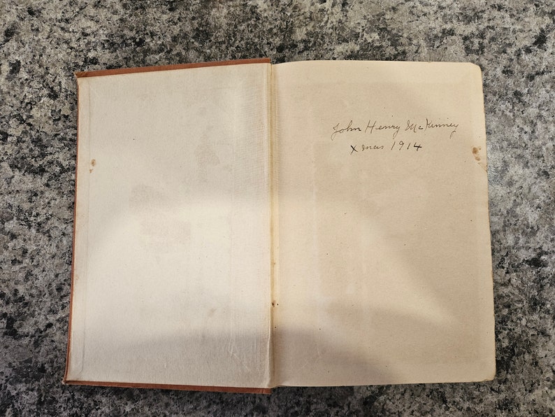 Puede incluir: Primer plano del interior de la cubierta de un libro con una inscripci&oacute;n manuscrita que dice "John Henry McKinney X-mas 1914".