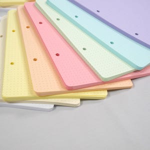 Könnte beinhalten: Eine Sammlung farbenfroher Notizbücher mit Punktraster in Pastelltönen von Weiß, Gelb, Pfirsich, Rosa, Grün, Blau und Lila. Jedes Notizbuch hat ein Loch zum Binden. Die Notizbücher sind aufgefächert und zeigen die Kanten und das Punktrastermuster.