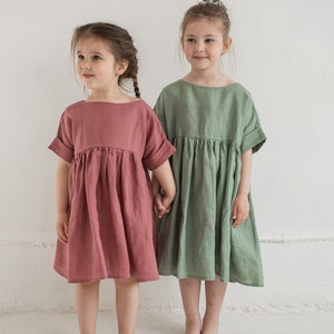Peut inclure: Deux robes à manches courtes avec une taille froncée et une encolure ronde. Une robe est de couleur rose vieux rose, et l'autre robe est de couleur vert sauge doux. Les deux vêtements présentent des manches à revers et une jupe ample.
