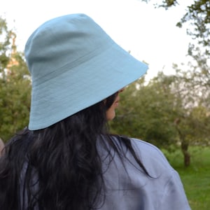 May include: A light blue bucket hat with a wide, downward-sloping brim and a rounded crown. The hat features visible stitching details along the brim and is constructed from a solid-colored fabric, providing a simple and functional head covering.