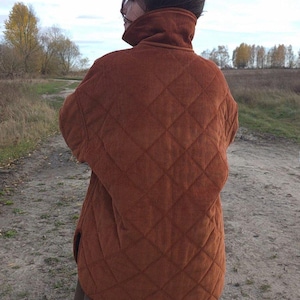 May include: A rust-colored quilted corduroy jacket with a high collar. The jacket features a diamond pattern and a relaxed fit, suitable for layering. The jacket is worn outdoors.
