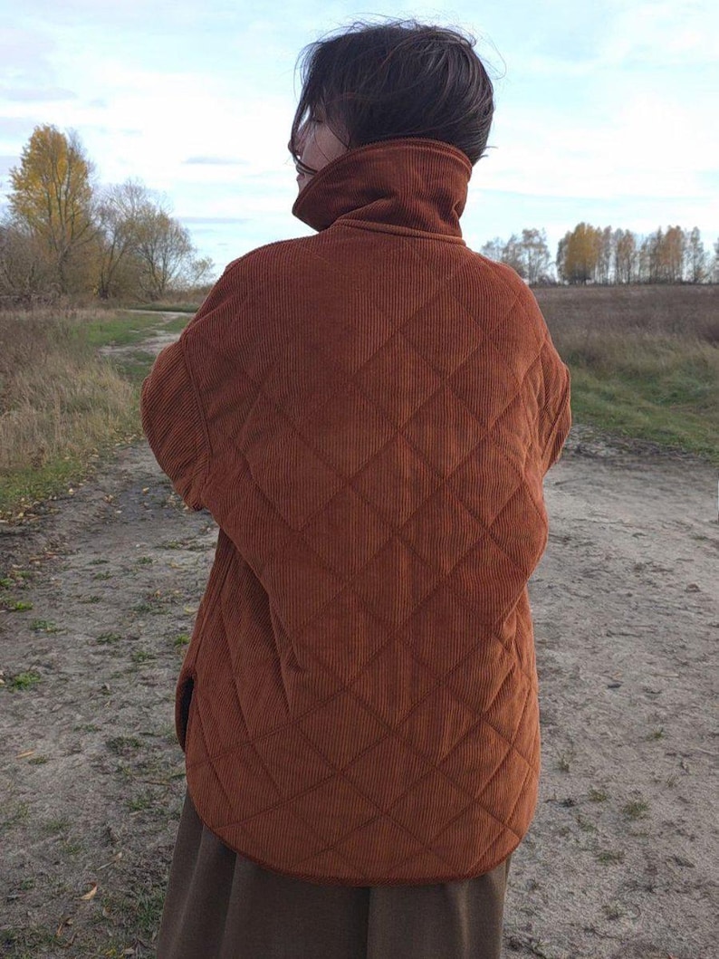 May include: A rust-colored quilted corduroy jacket with a high collar. The jacket features a diamond pattern and a relaxed fit, suitable for layering. The jacket is worn outdoors.