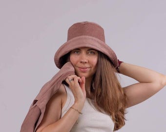 May include: A dusty rose corduroy bucket hat with a matching jacket. The hat has a wide brim and a rounded crown. The jacket is draped over the shoulder. The person is wearing a white tank top.