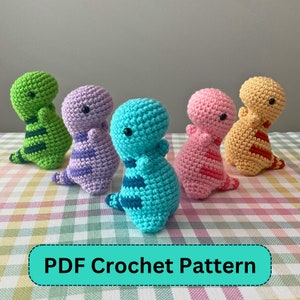 Op de afbeelding: Vijf kleurrijke gehaakte dinosaurussen in groen, paars, blauw, roze en geel. Elke dinosaurus heeft een gestreept patroon en kleine zwarte ogen. De tekst "PDF Crochet Pattern" staat onderaan.