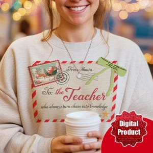 May include: A light beige sweatshirt with a festive design. The graphic includes a postage stamp with Santa and reindeer, a green bow, and the text "From: Santa To: the Teacher who always turn chaos into knowledge."
