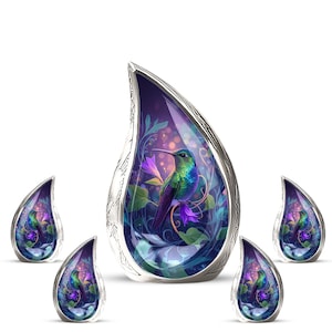 May include: A collection of teardrop-shaped pendants with a silver-colored frame. Each pendant features a vibrant image of a hummingbird perched among purple flowers and foliage, set against a dark purple background. The pendants are designed with intricate details.
