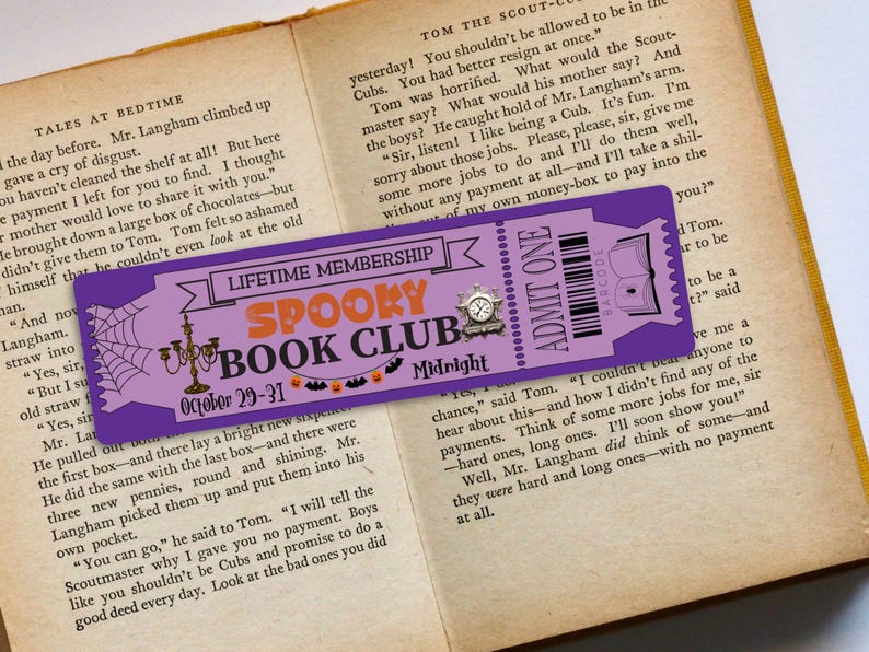 May include: A purple and white bookmark with a spiderweb design and the text "Lifetime Membership Spooky Book Club October 29-31 Midnight". The bookmark also has a ticket with the text "Admit One" and a barcode.