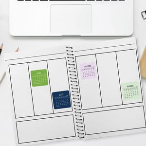 May include: A spiral-bound planner open to a blank weekly layout with four small adhesive calendar stickers attached to the pages. The stickers are labeled June in green, May in dark blue, October in light purple, and March in light green.