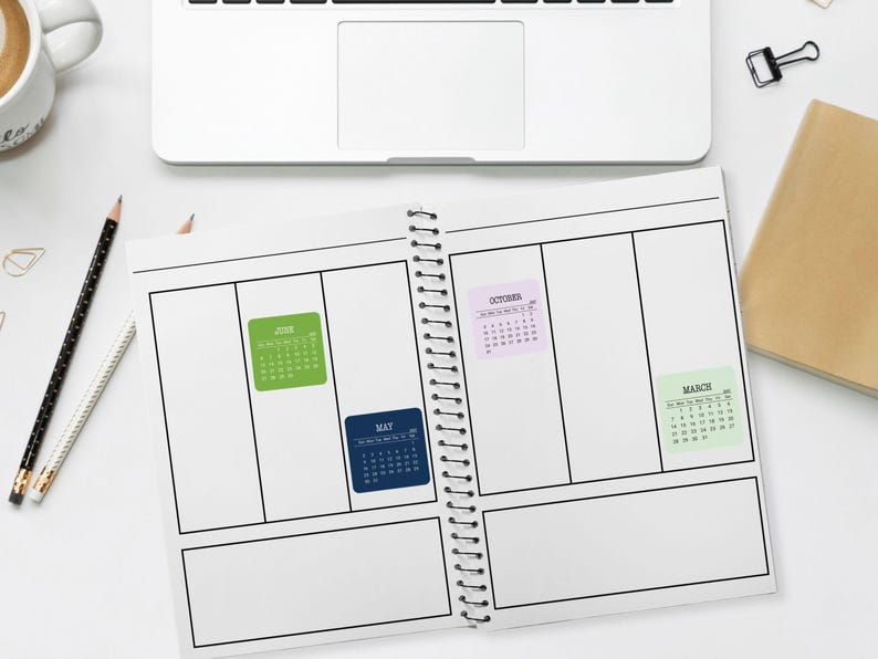 May include: A spiral-bound planner open to a blank weekly layout with four small adhesive calendar stickers attached to the pages. The stickers are labeled June in green, May in dark blue, October in light purple, and March in light green.