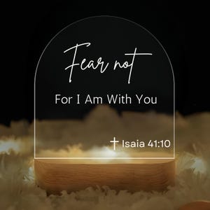 May include: A white acrylic sign with a rounded top and a wooden base. The sign reads "Fear not, For I Am With You" and includes a cross and the scripture reference "Isaiah 41:10".