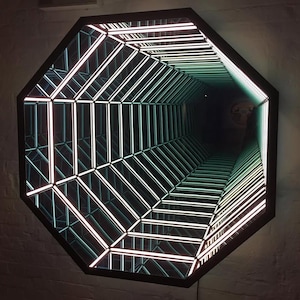 Puede incluir: Un espejo octogonal con marco negro, con un diseño geométrico de luces de neón blancas y verdes que crean una ilusión de profundidad. Las luces forman una perspectiva de túnel, con un interior oscuro.