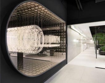 May include: A large, oval-shaped wall installation featuring a series of repeating, illuminated white neon letter R shapes layered to create a tunnel effect. The installation is set within a dark, matte black wall, contrasting with the bright white light.