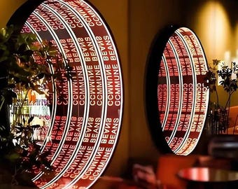 May include: Two circular infinity mirrors with black frames featuring the repeating white text COMMUNE BEANS. The mirrors create a deep, tunnel-like visual effect with concentric rings of light and text, reflecting a warm, dimly lit interior space.