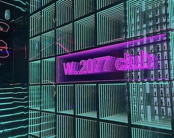 May include: A wall installation featuring a grid of square panels with glowing teal neon light frames creating an infinite tunnel effect. A bright pink neon sign in the center displays the text W.2077 club, set against a dark background.