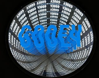 May include: A circular infinity mirror featuring the word GOOEY in a bright blue, wavy, three-dimensional font. The interior of the mirror displays a repeating, receding pattern of the word GOOEY in white text against a dark background.