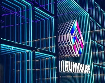 May include: A wall display featuring a grid of black frames illuminated by bright cyan and blue neon light strips that create a tunnel effect. A central geometric logo with a gradient of pink and blue sits above the white text FUNHOUSE.