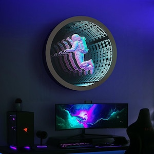 Pode incluir: Um espelho infinito circular montado na parede com um gráfico central de um astronauta flutuando no espaço. O design cria um efeito de túnel repetitivo com iluminação LED azul e roxa, exibindo uma ilusão de profundidade da figura.