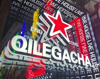 May include: A three-dimensional illuminated sign featuring a red star above the white text QILEGACHA. The background consists of a dark surface with repeating white text that reads LIVE HOUSE, creating a layered and high-contrast visual effect.