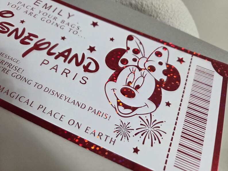 May include: A white ticket with red accents and glitter, featuring the text "Disneyland Paris" and a Minnie Mouse illustration. The ticket includes the text "Pack your bags, you are going to..." and "Magical place on Earth."