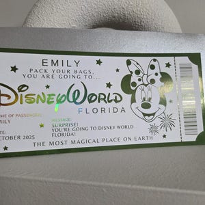 May include: A Disney World ticket-themed card with a green border, featuring the Disney World logo and a Minnie Mouse illustration. The card includes the name "EMILY" and the message "SURPRISE! You're going to Disney World Florida!"