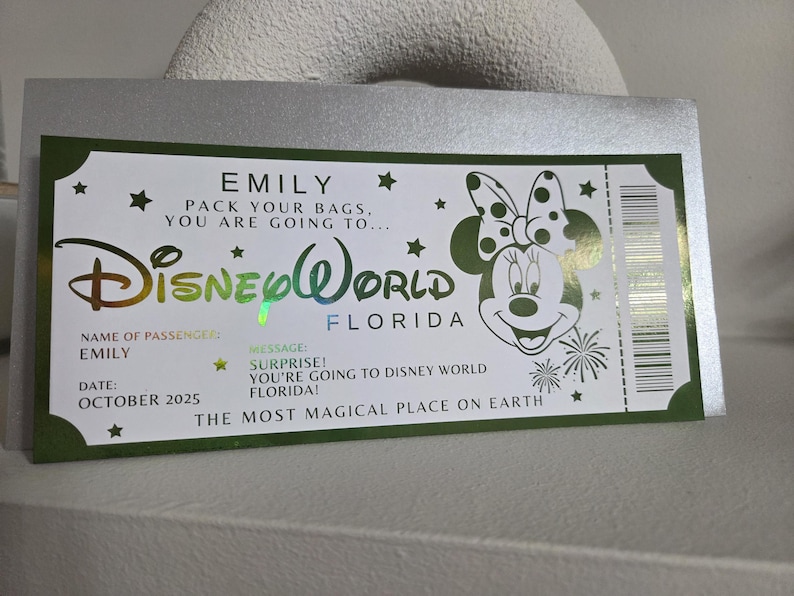 May include: A Disney World ticket-themed card with a green border, featuring the Disney World logo and a Minnie Mouse illustration. The card includes the name "EMILY" and the message "SURPRISE! You're going to Disney World Florida!"