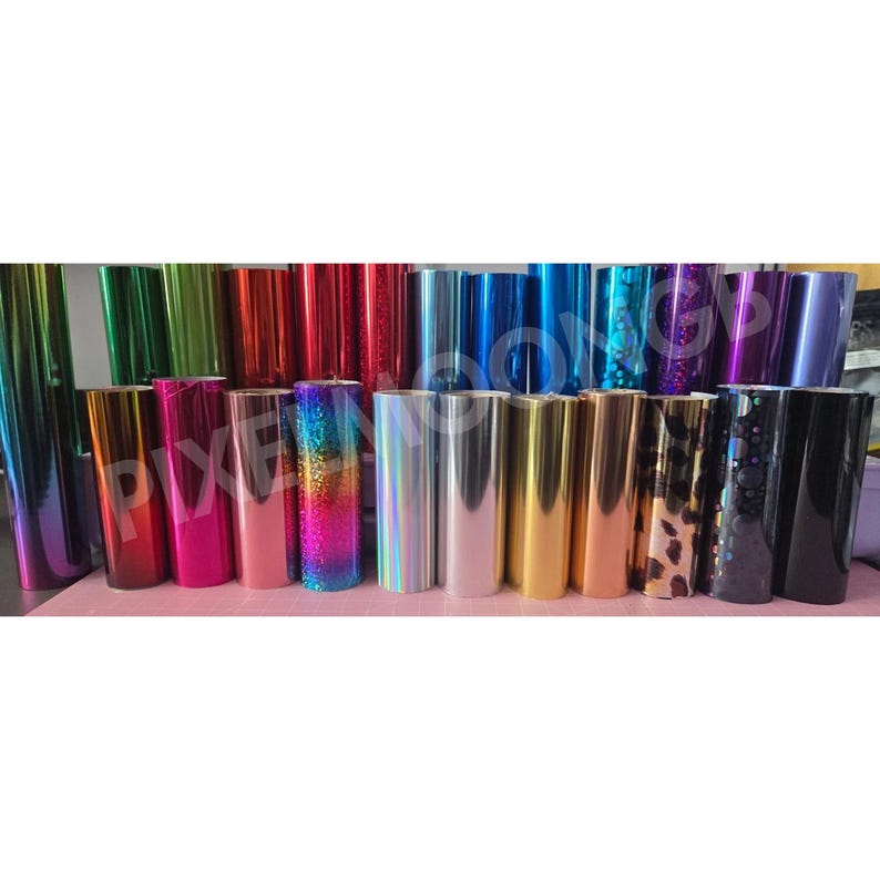 May include: A collection of colorful vinyl rolls in various shades, including green, red, blue, and gold. Some rolls have glitter or holographic effects. The rolls are arranged in rows, showcasing a variety of colors and textures.