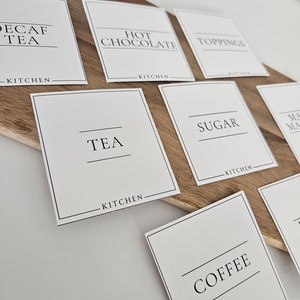 K&ouml;nnte beinhalten: Wei&szlig;e quadratische Etiketten mit schwarzem Text f&uuml;r eine K&uuml;chengetr&auml;nke-Station. Die Etiketten lauten "Kaffee ohne Koffein", "Hei&szlig;e Schokolade", "Toppings", "Tee", "Zucker", "Kaffee".