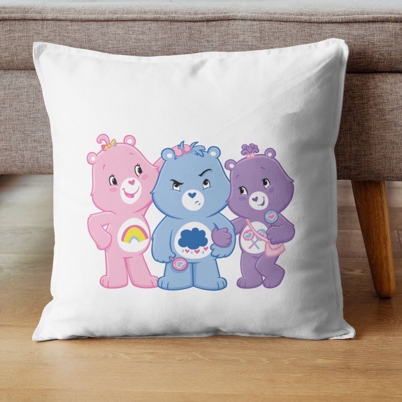 May include: Three Care Bears, a pink bear with a rainbow, a blue bear with a cloud, and a purple bear with a heart, are standing together on a white pillow.