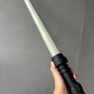 May include: A black lightsaber with a white glow stick. The lightsaber is made of plastic and has a textured surface.