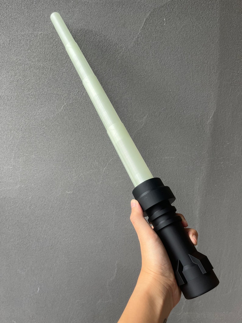 May include: A black lightsaber with a white glow stick. The lightsaber is made of plastic and has a textured surface.