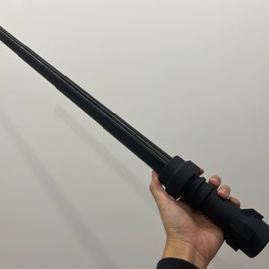 May include: A black telescopic baton with a textured grip. The baton is fully extended and appears to be made of metal.
