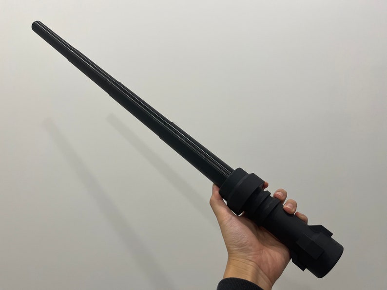 May include: A black telescopic baton with a textured grip. The baton is fully extended and appears to be made of metal.