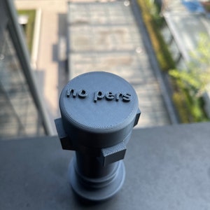 May include: A gray 3D printed object with the words "no pers" on top. The object has a cylindrical shape with a square base.